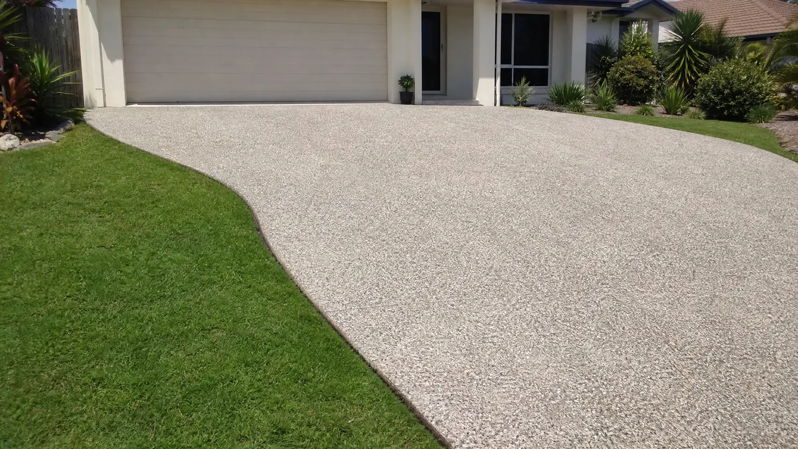 Clean and well-maintained exposed aggregate concrete driveway with fresh sealer coating on a bright sunny Gold Coast afternoon