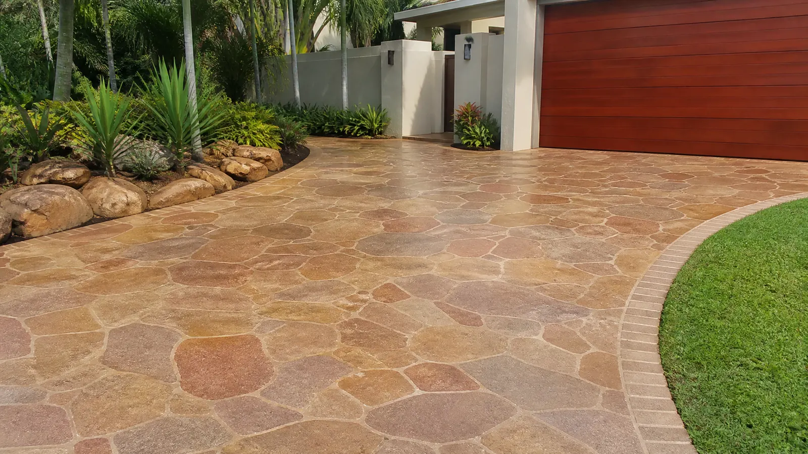 Completed spray-on concrete resurfacing with random stone pattern in sandstone colour on a Gold Coast driveway with landscaping
