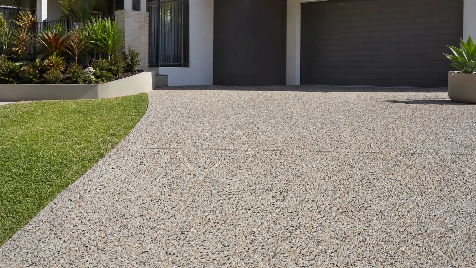 Exposed aggregate concrete driveway with natural stone textures and warm earth tones on a Gold Coast property with palm trees