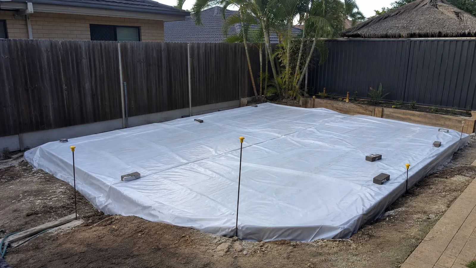 Freshly poured and finished concrete slab curing under plastic sheeting with expansion joints visible on Gold Coast building site