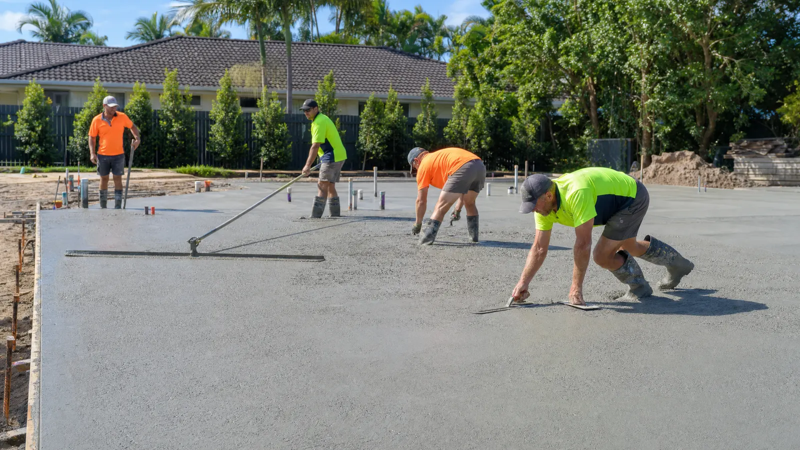 Professional concreters finishing a large residential concrete slab with power trowels on a Gold Coast building site at sunrise