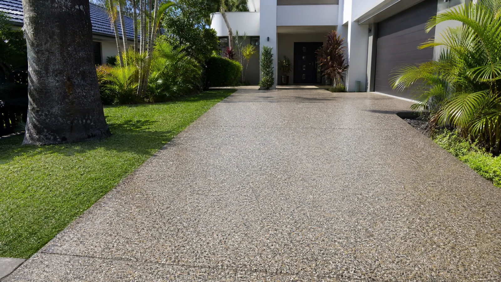 Sealed exposed aggregate driveway with natural stone textures glistening under sunlight outside a contemporary Gold Coast residence