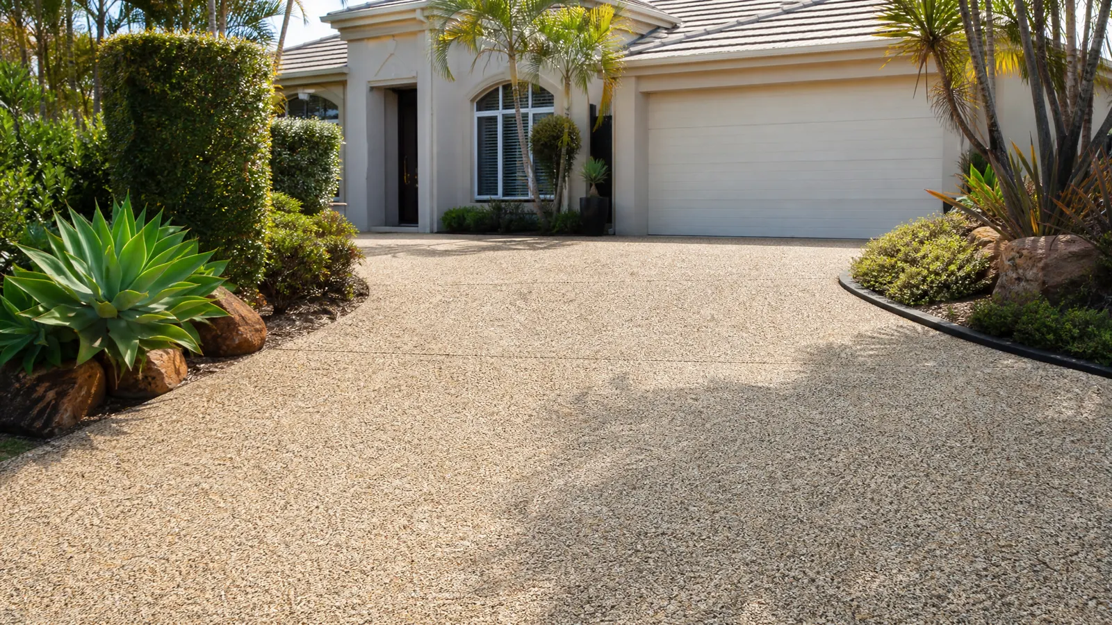 Warm sandstone exposed aggregate driveway with cream and gold stone blend complementing a white rendered Gold Coast home