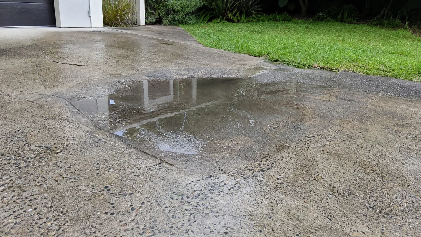 Water pooling on an uneven concrete driveway surface after heavy rainfall showing poor drainage and surface deterioration